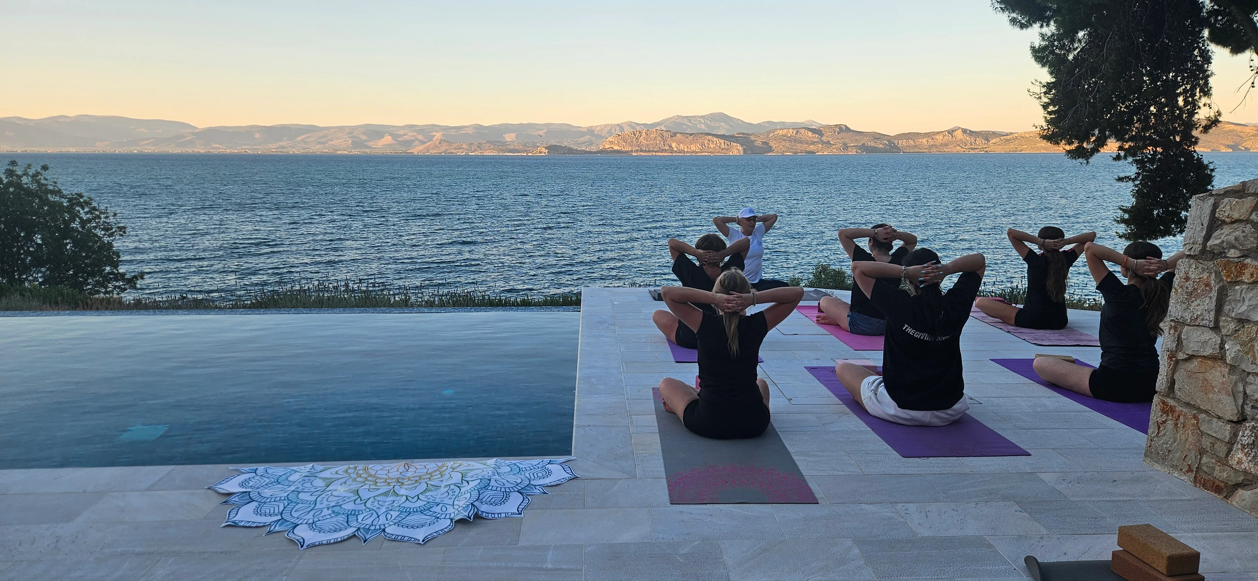 Yoga group seated on mats by the infinity pool at dusk