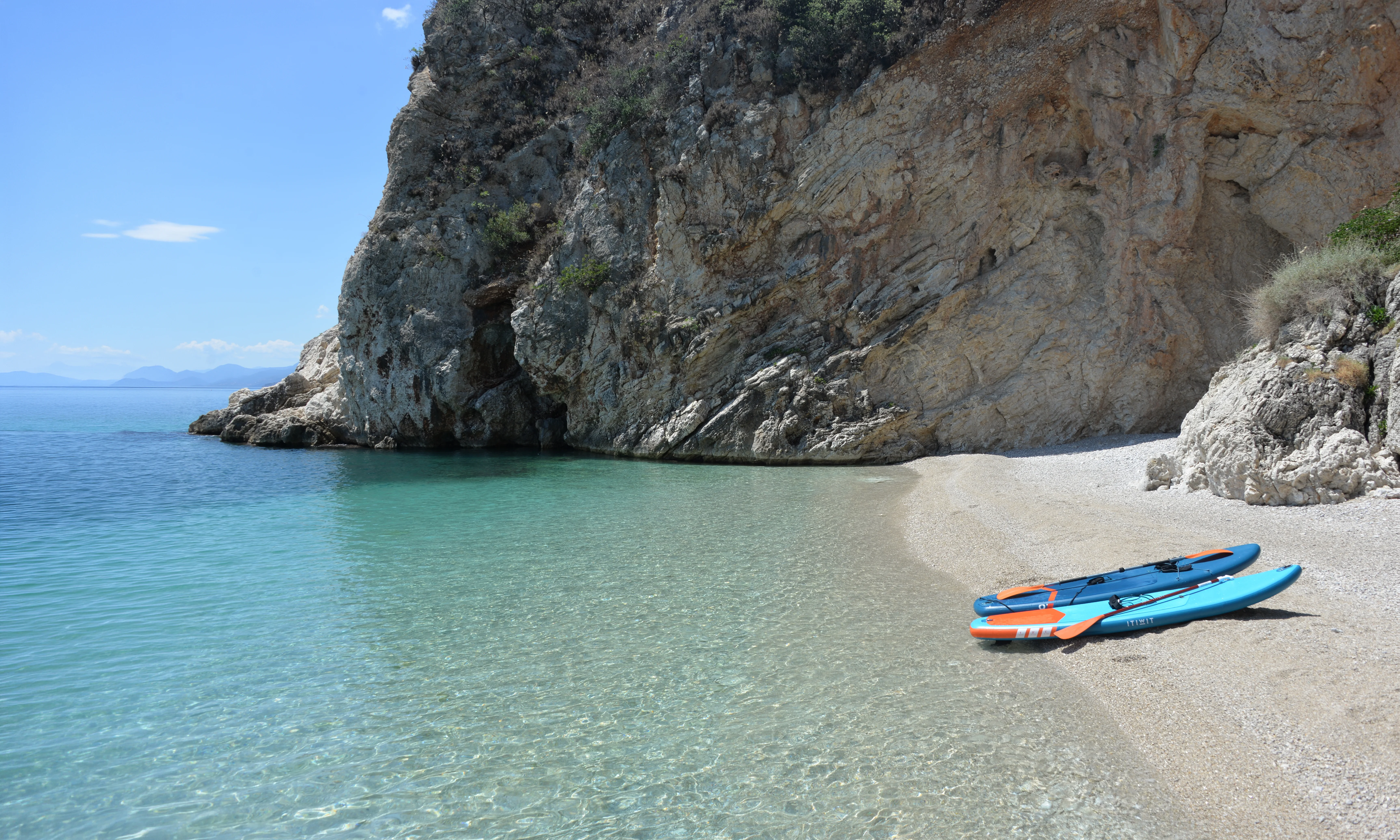 Pebble cove with clear turquoise water and two paddleboards on the beach