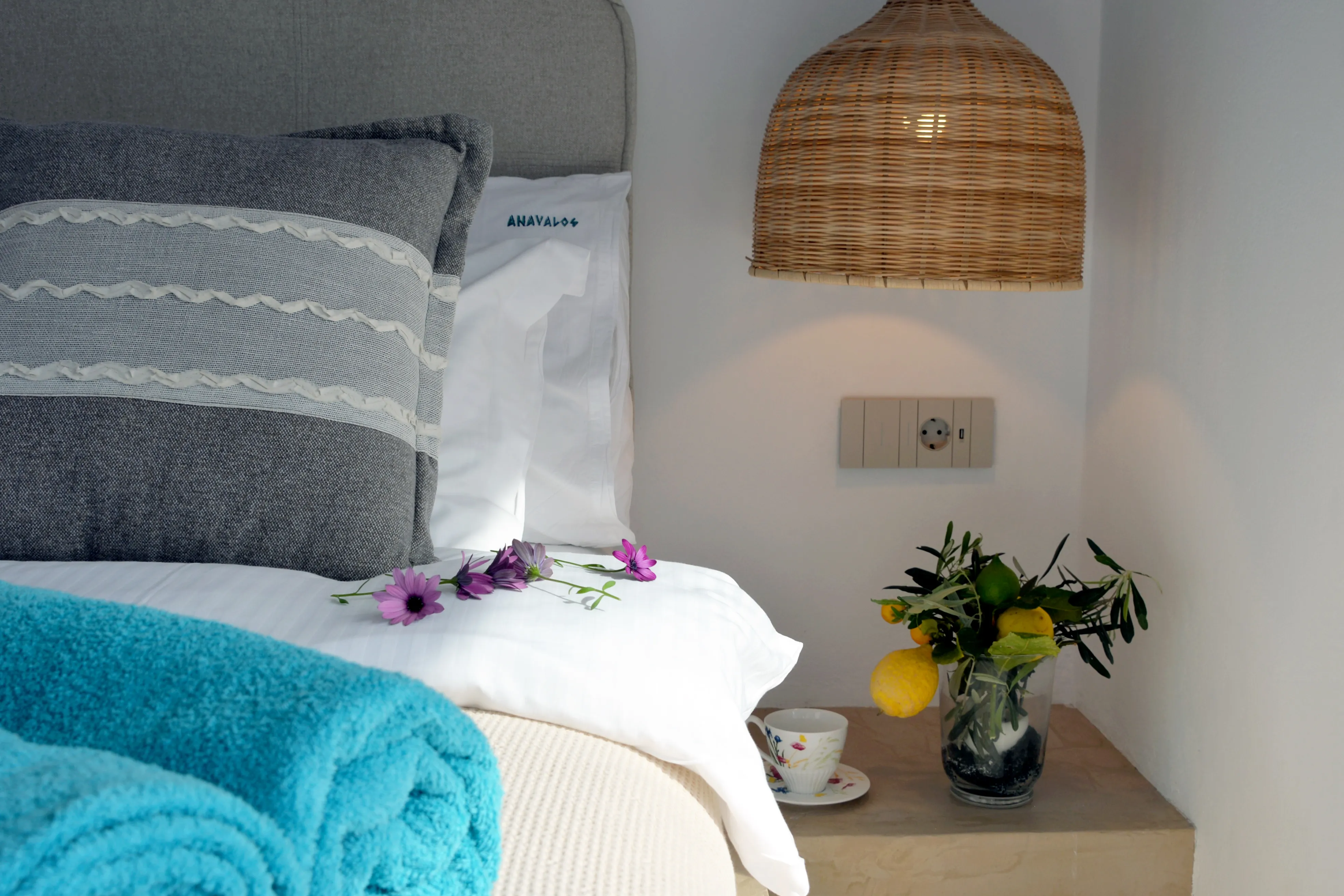 Bedside of Euros with wicker pendant, flowers and a turquoise towel