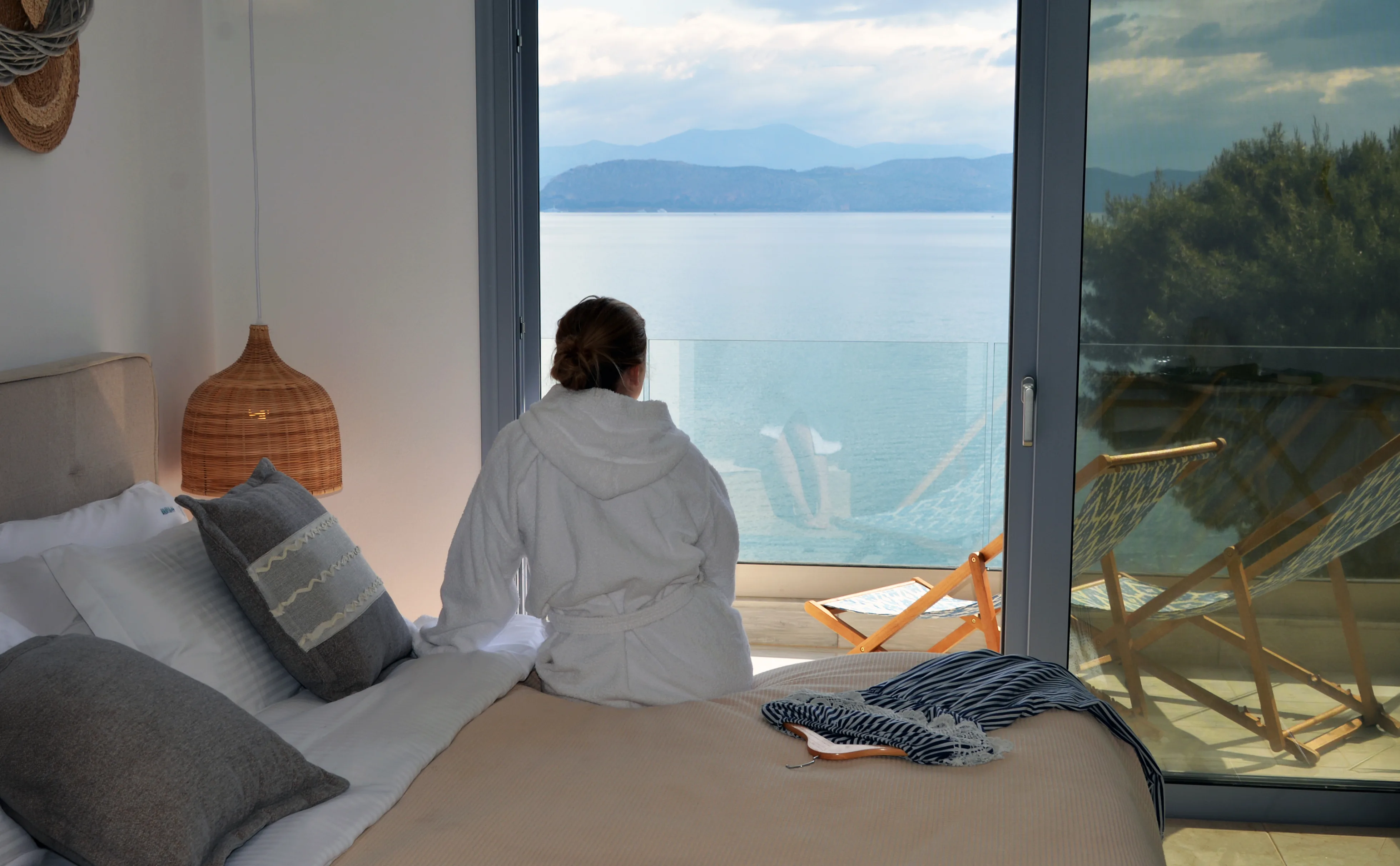 Guest sitting on the bed, looking through the open glass door to the sea