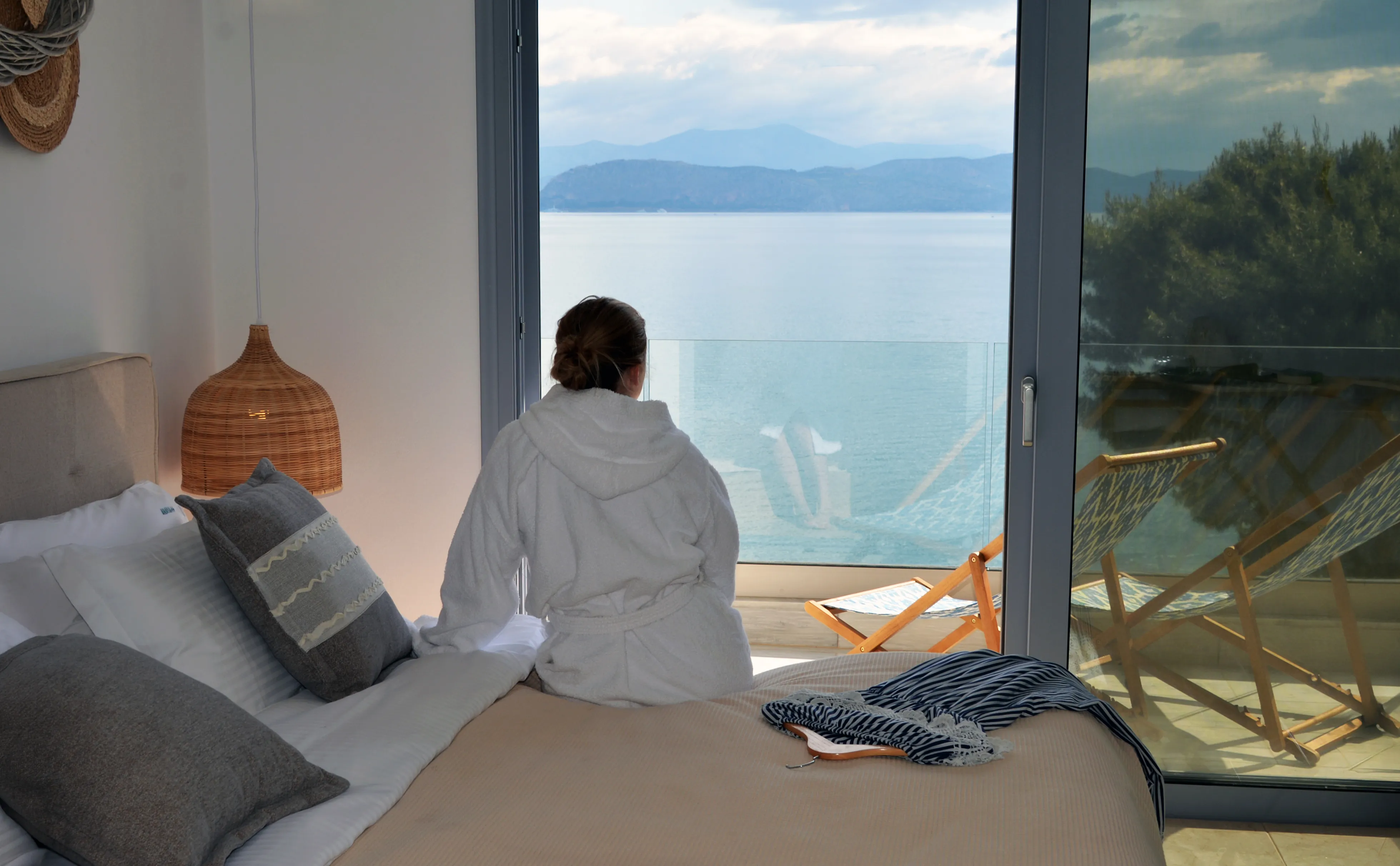 Guest sitting on the bed, looking through the open glass door to the sea