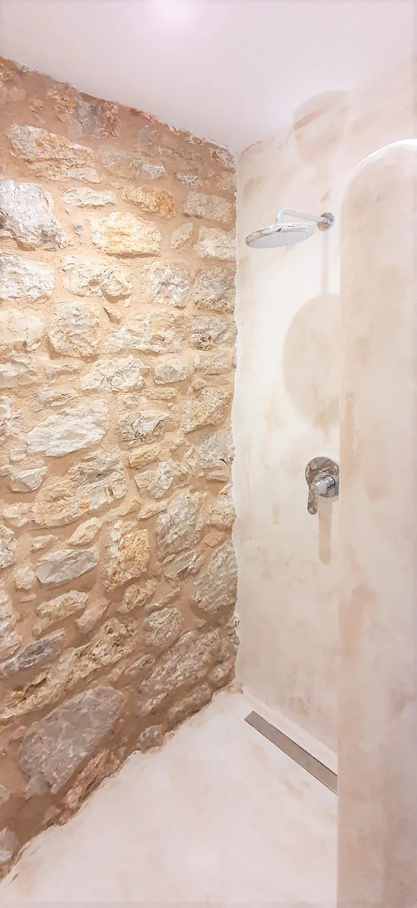 Dusche mit Natursteinwand und polierten Armaturen