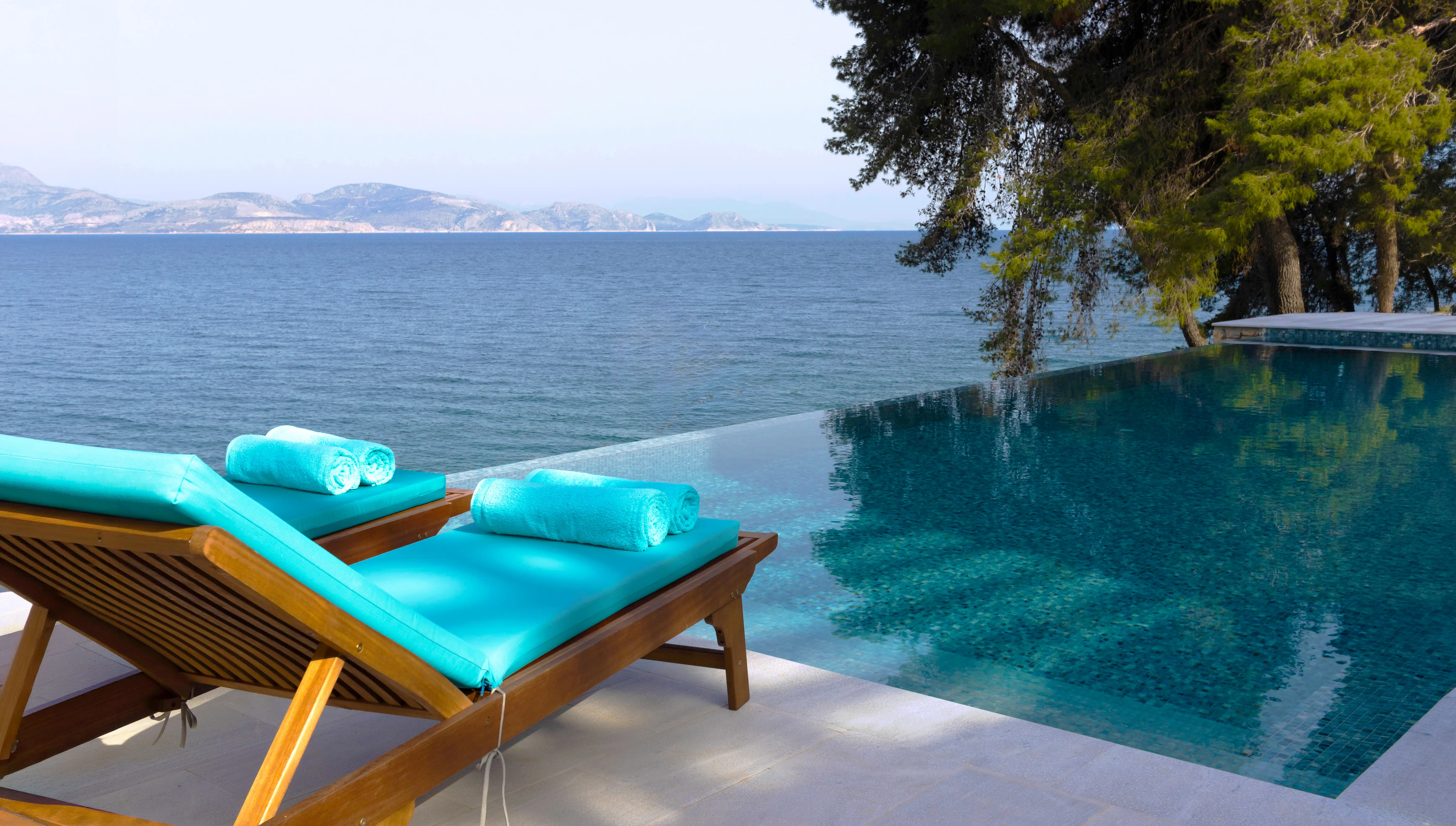 Turquoise loungers beside the infinity pool facing the Argolic Gulf and mountains