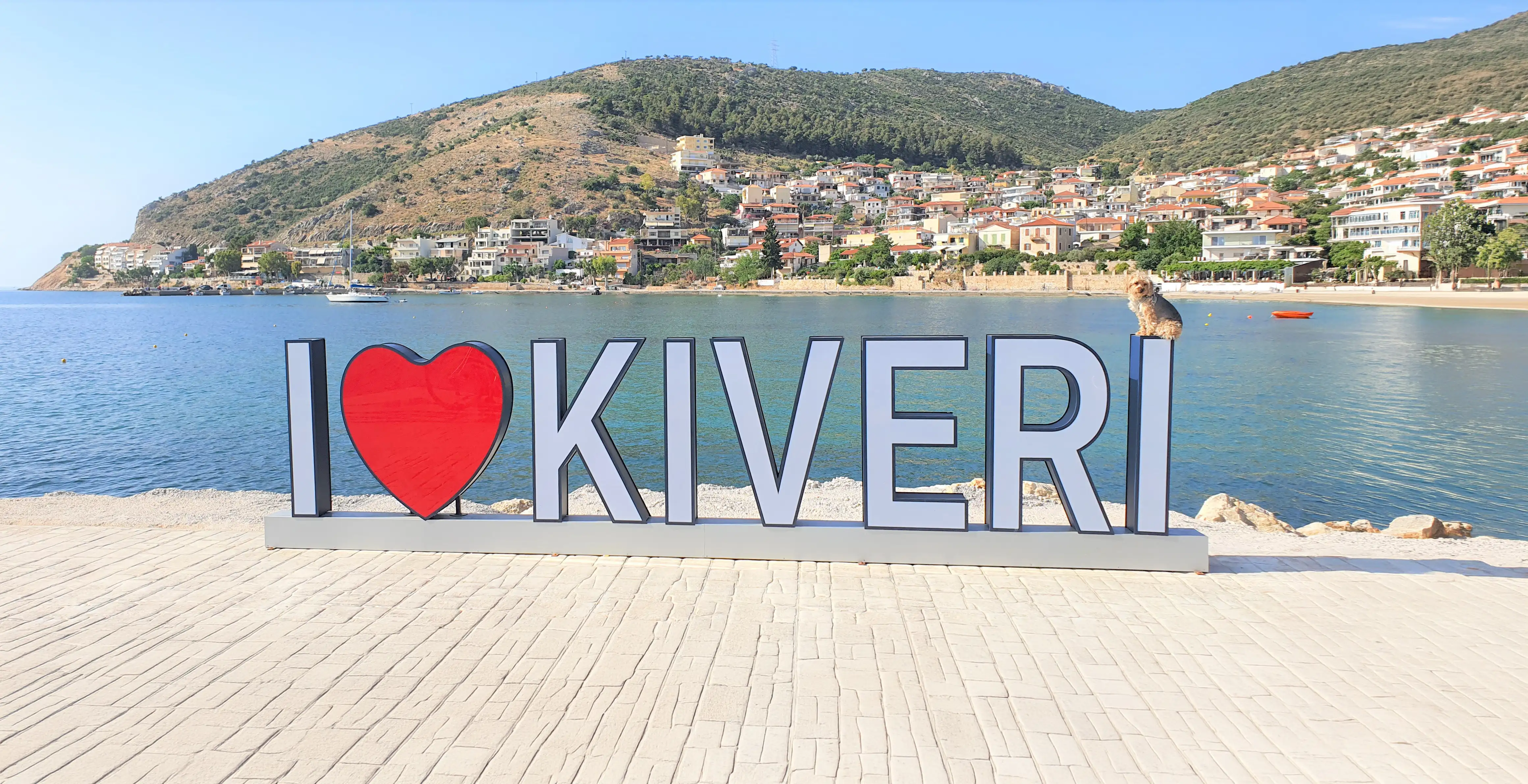 Der Schriftzug „I love Kiveri“ an der Uferpromenade des Dorfes, dahinter Häuser am Hang