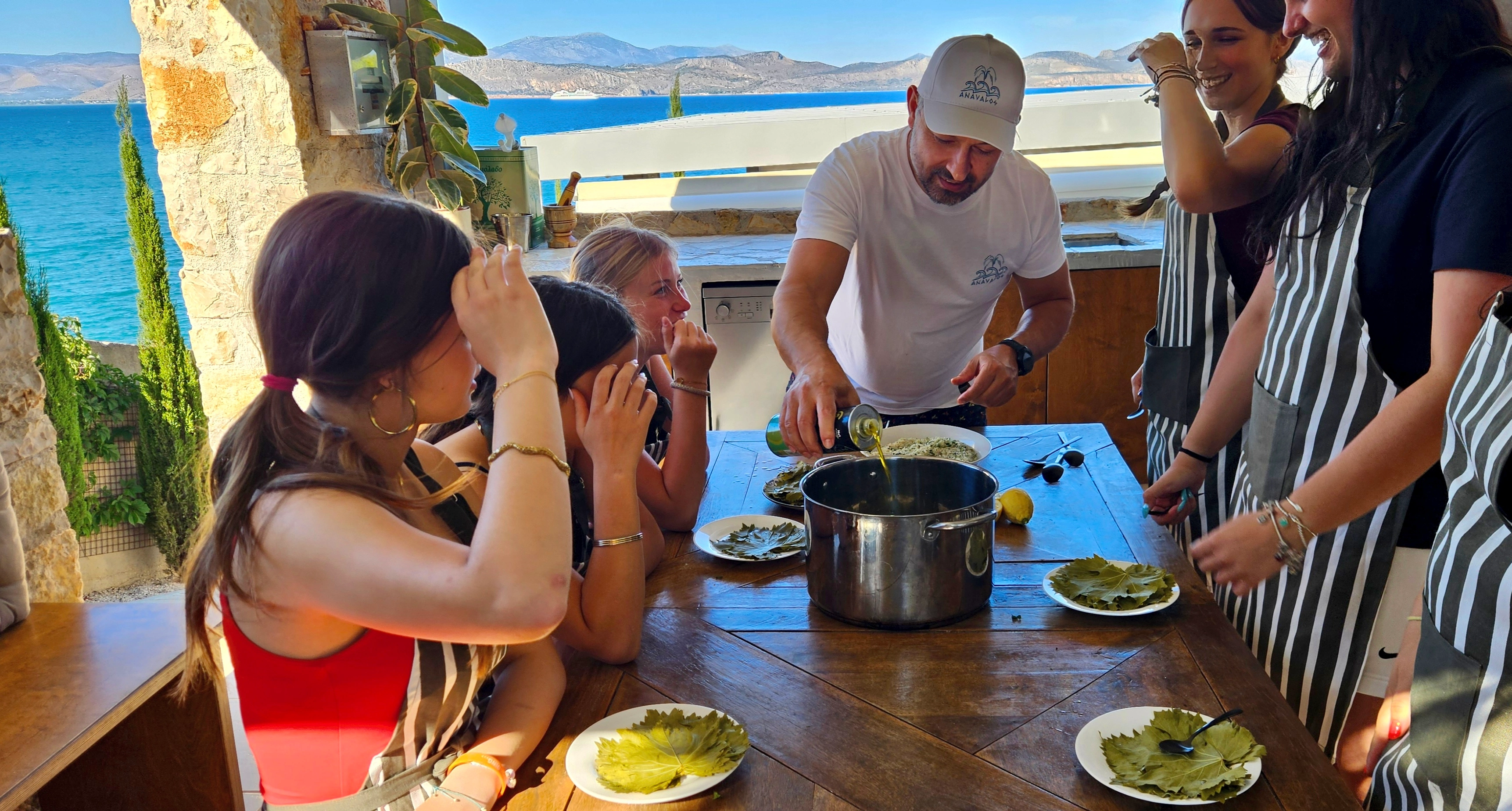 Guests learning Greek cooking together on the sea-view terrace